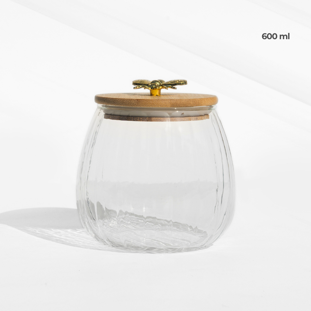 A set of two fluted borosilicate glass storage jars with airtight wooden lids featuring gold butterfly knobs, placed on a matching wooden tray for elegant storage.